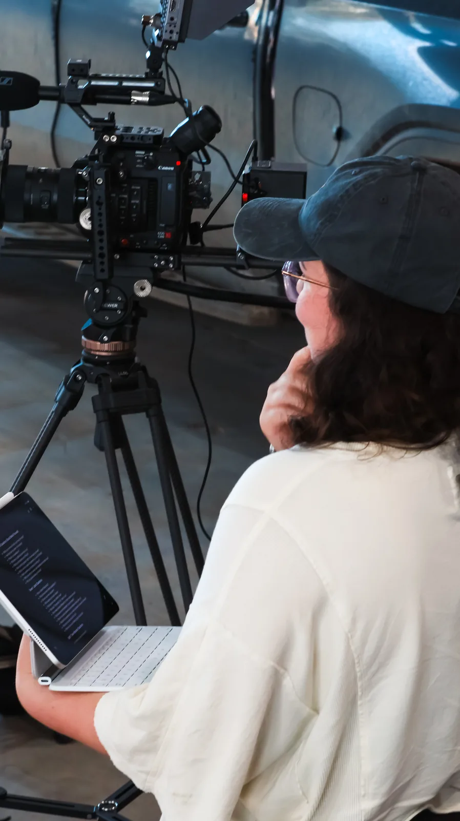 Crew member seated behind a tripod-mounted camera reviewing a script on a tablet