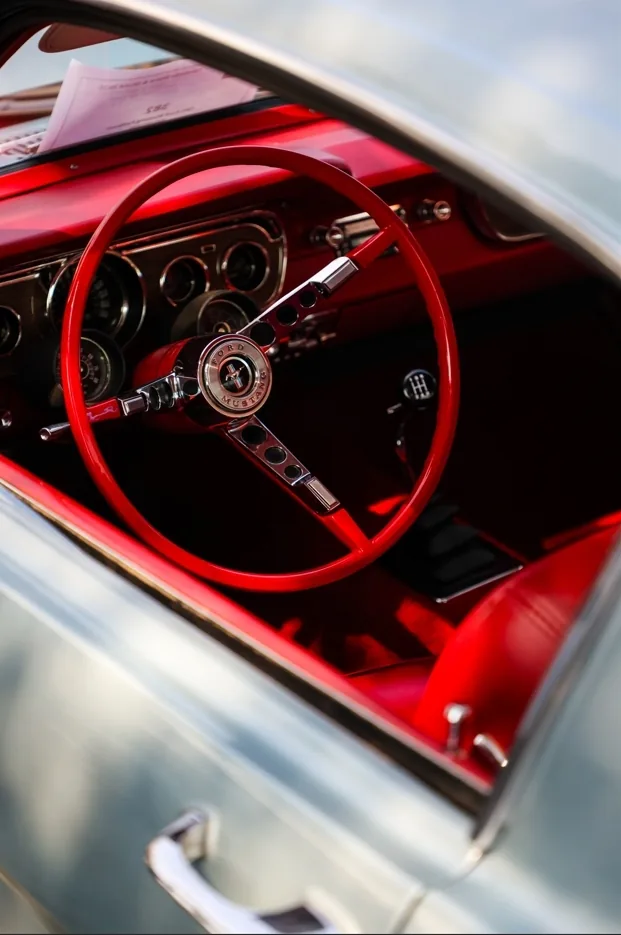 Red steering wheel and dashboard of a classic car seen through the side window