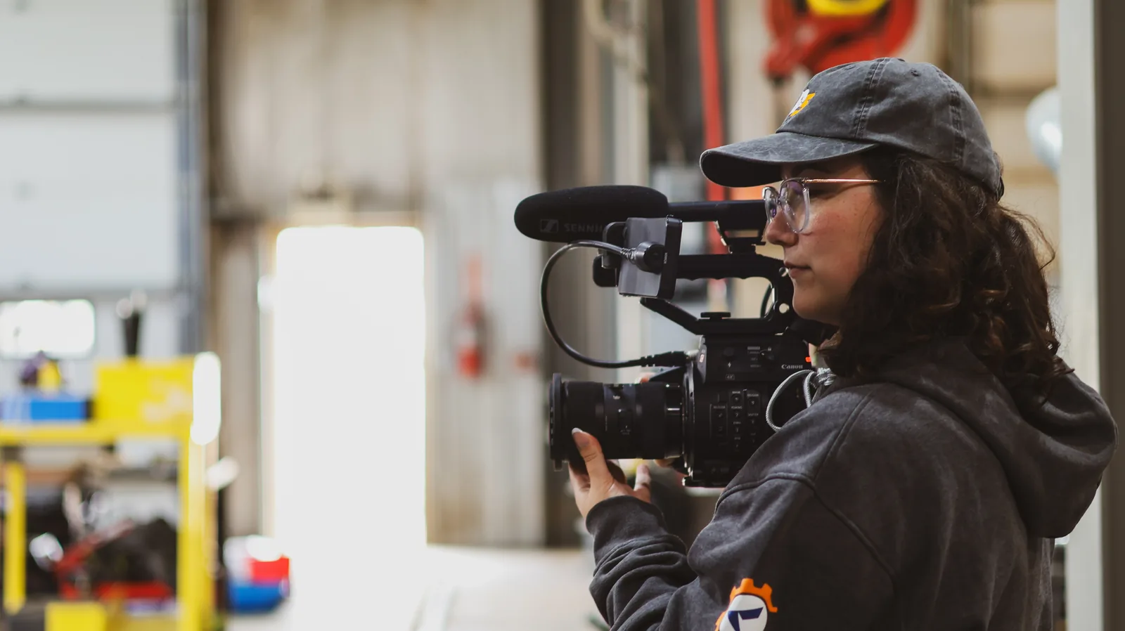 Camera operator shooting with a shoulder-mounted cinema camera in a shop bay