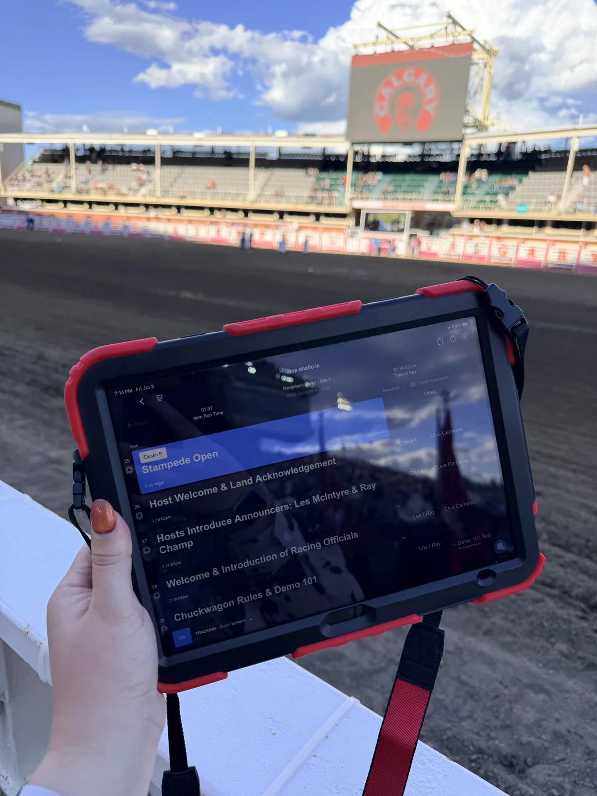 Tablet showing a live show rundown held up in front of a grandstand track
