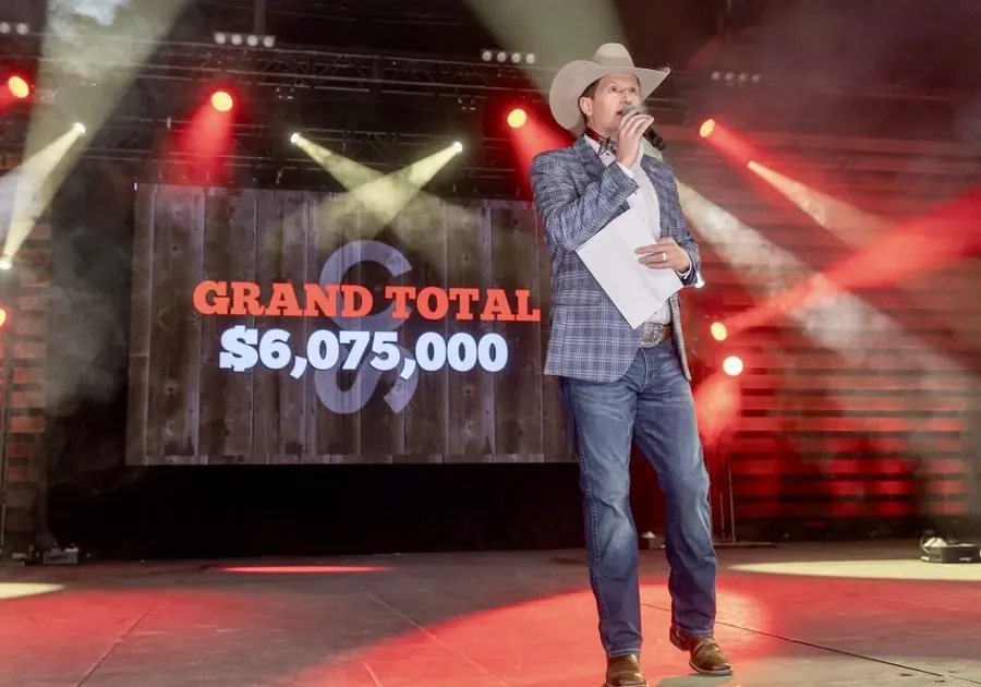 Host on stage in front of a screen showing the auction grand total